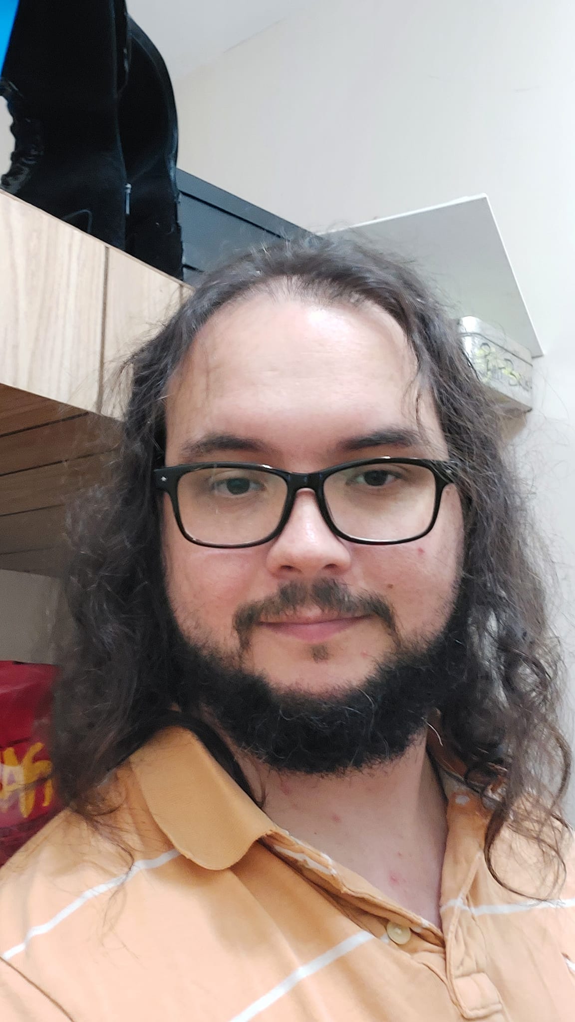 A man with long dark hair and a beard stands in a well lit room